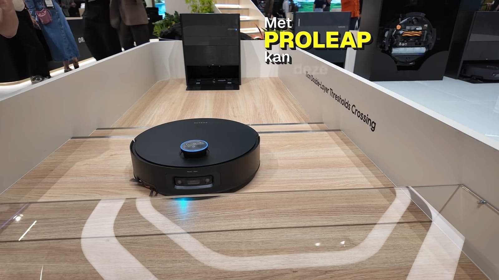 Zwarte Dreame robotstofzuiger rijdt in een testbak met houten vloer over een drempel, met de tekst Met ProLeap kan