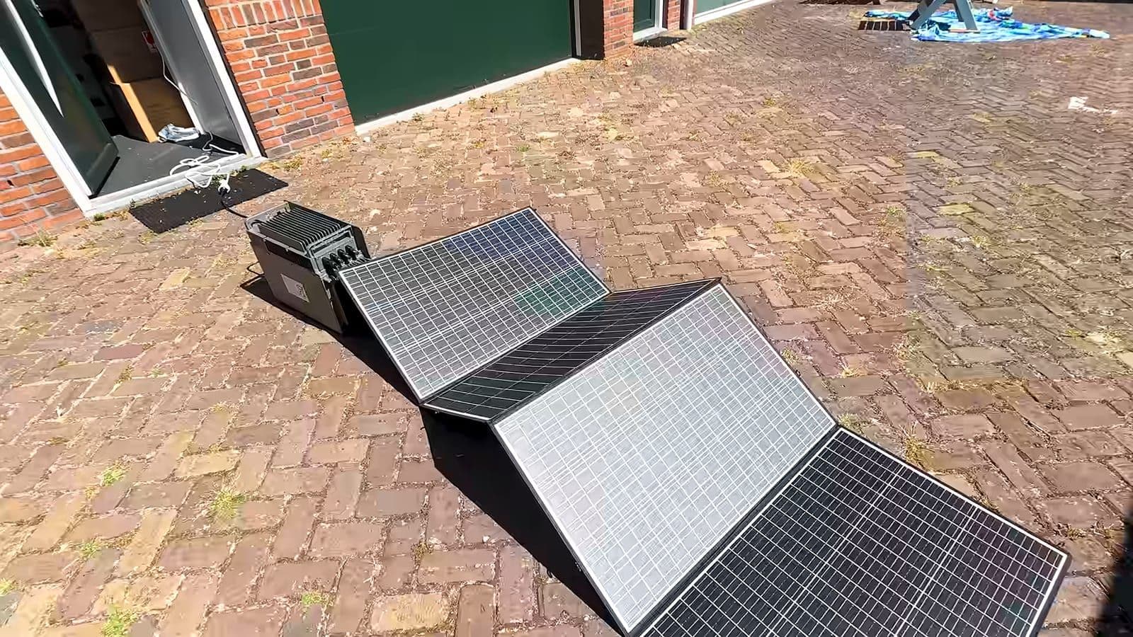 Opvouwbare zonnepanelen op een bestrate oprit, aangesloten op de Hoymiles-batterij naast een openstaande deur